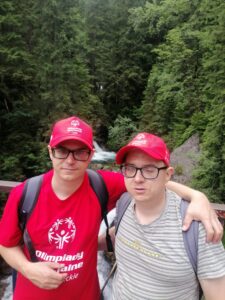 Dwóch młodych mężczyzn w czapkach i okularach na tle i drzew.