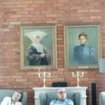 Mężczyzna i kobieta siedzący na tle ceglanej ściany z dwoma starymi portretami kobiet